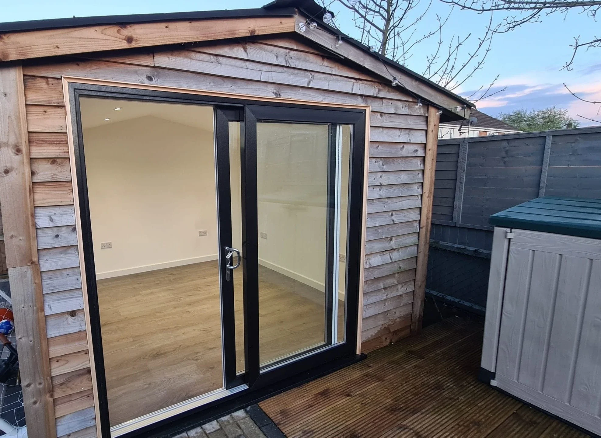 Dark uPVC sliding patio doors fitted to a timber-clad garden room