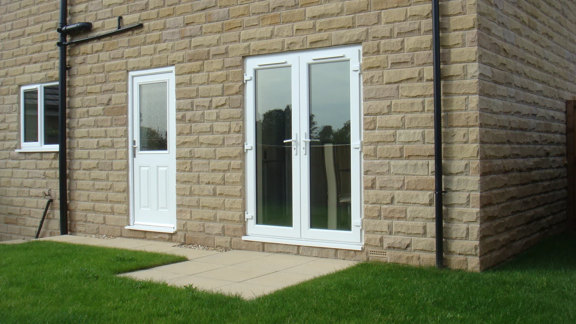 White uPVC French doors with fanlights on a stone-clad home