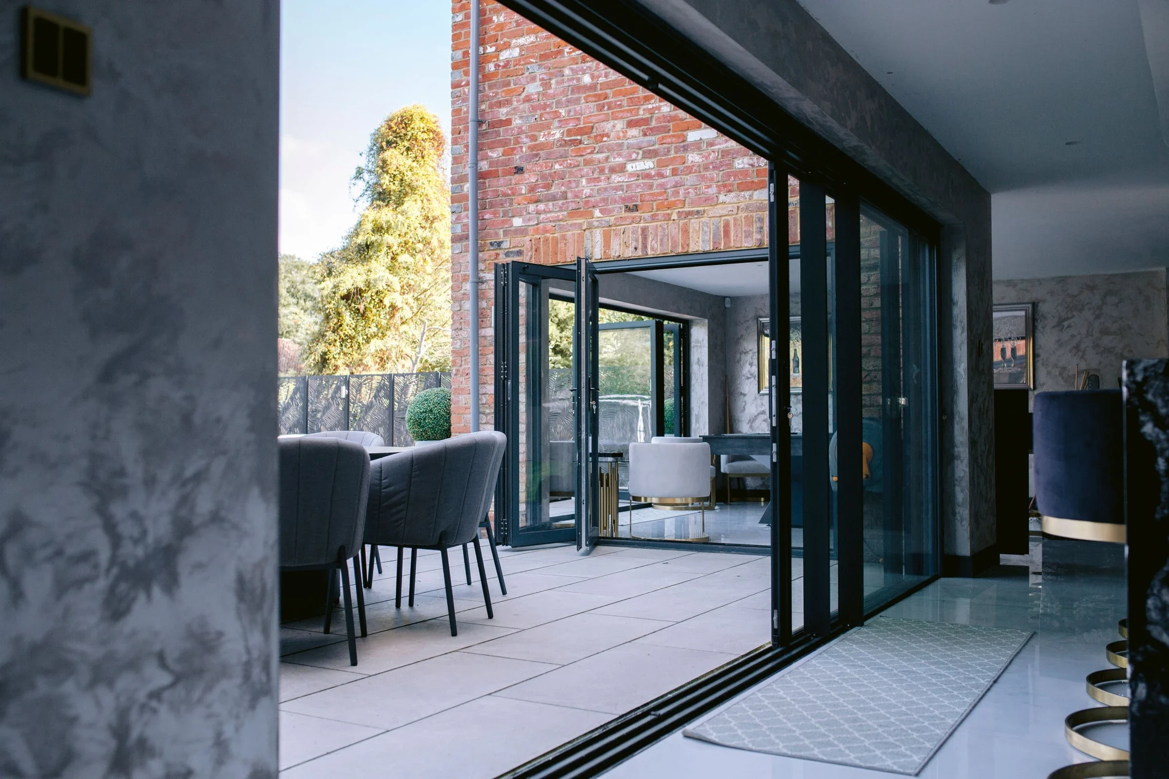 View through an open aluminium bifold doorway to a brick garden extension