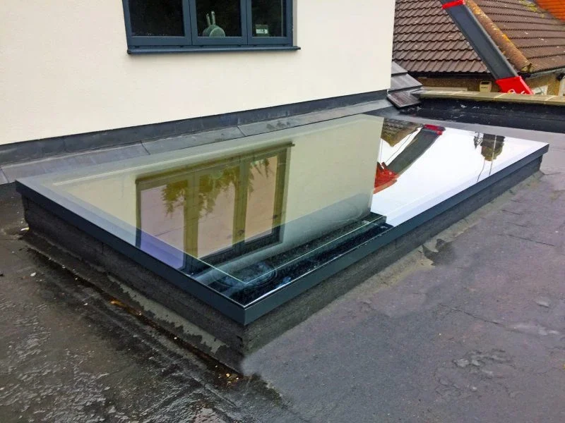 Flat rooflight reflected against the windows of an existing house