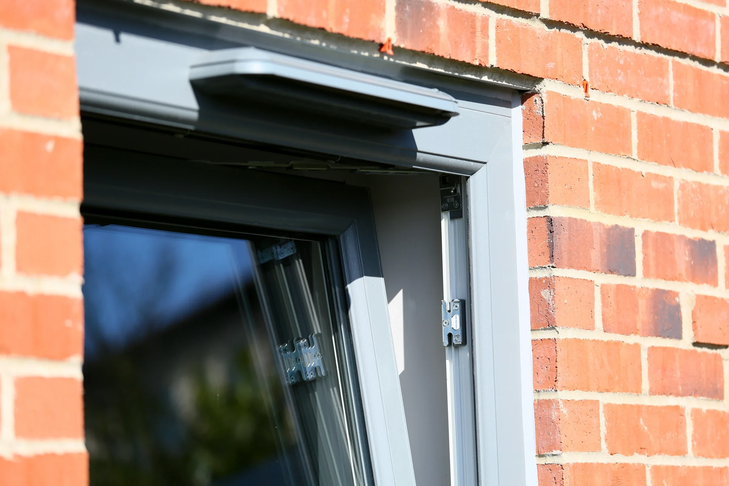 Grey uPVC tilt-and-turn window tilted inward in a brick reveal