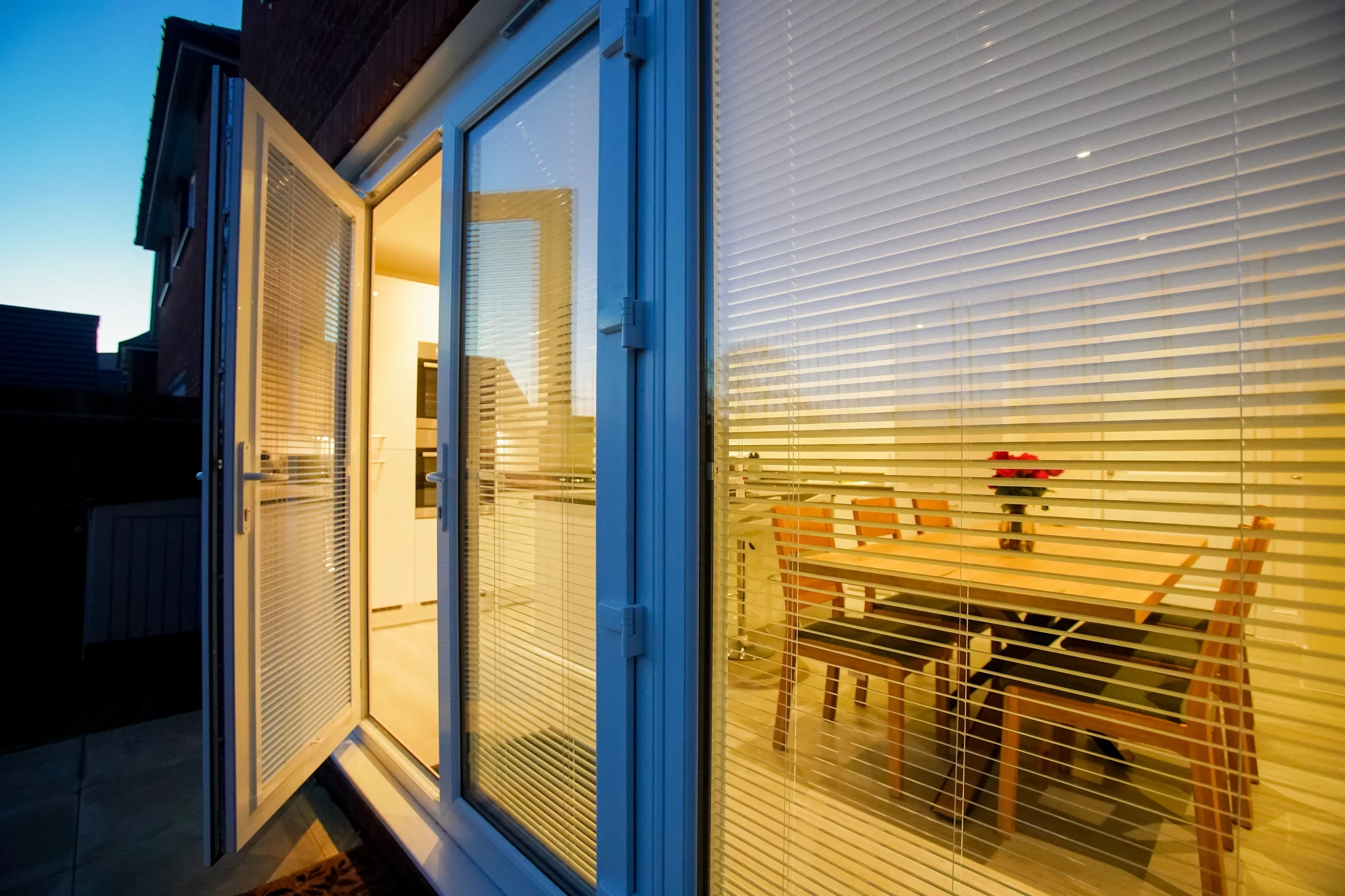 White uPVC French doors opening onto a timber deck at dusk
