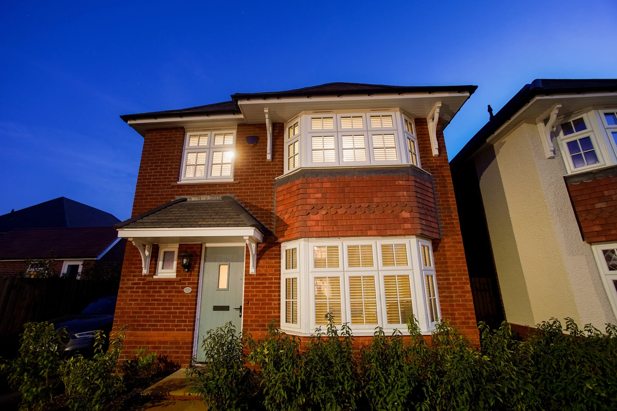 White uPVC bay windows on a red-brick detached house at dusk