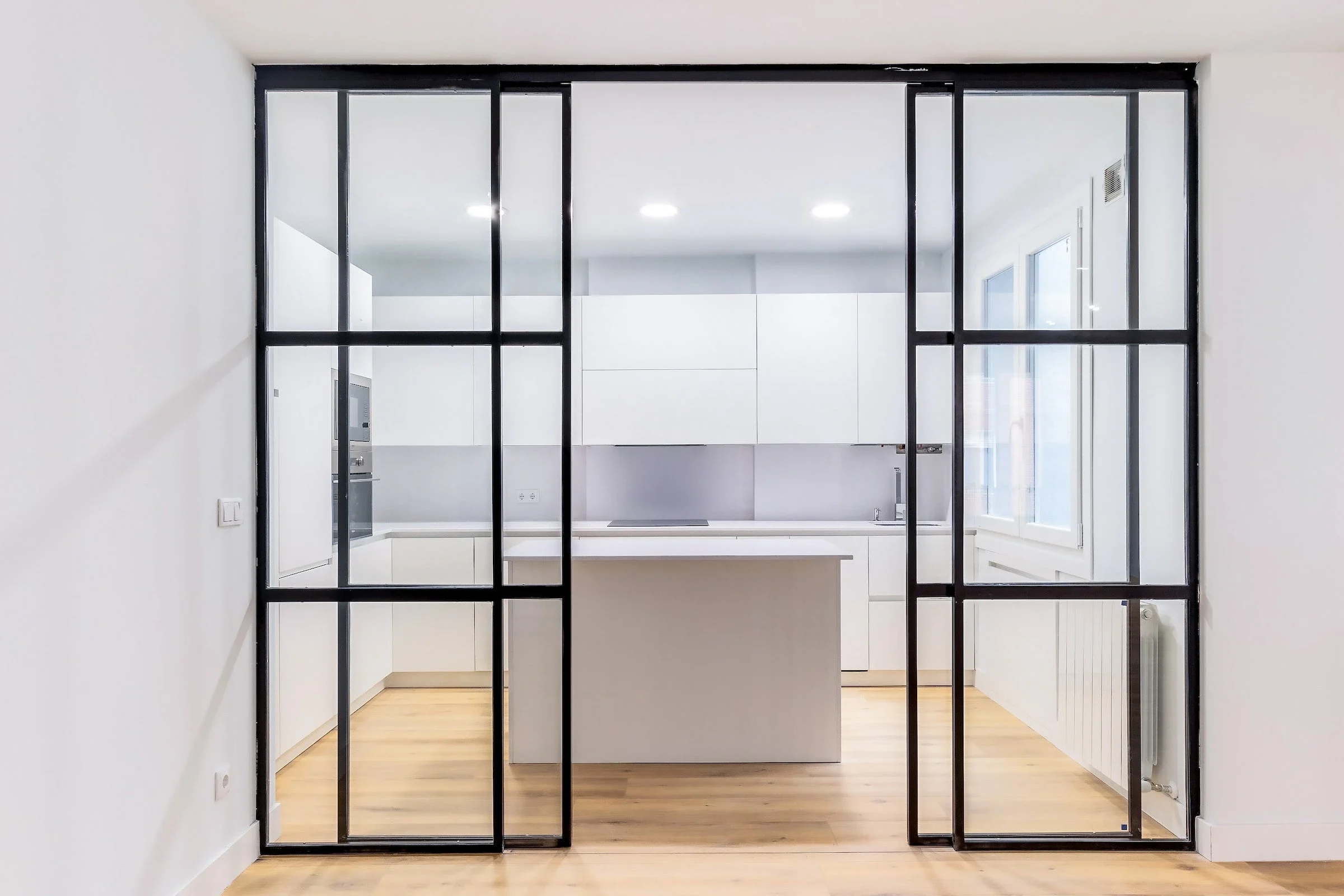 Black internal aluminium sliding doors opening into a white kitchen