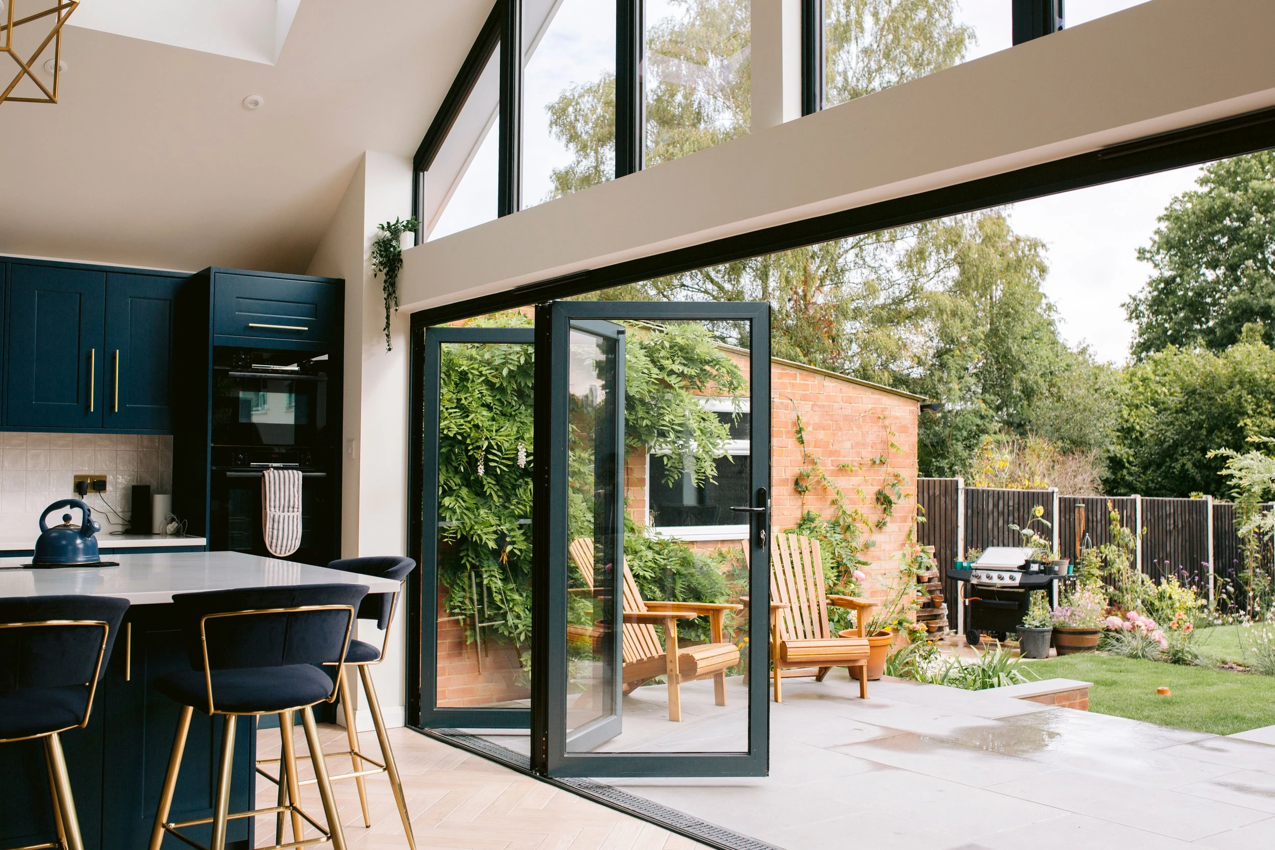 Open aluminium bifold doors connecting a navy kitchen with a garden patio