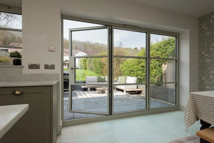 Pale grey heritage-style bifold doors opening from a kitchen to a patio