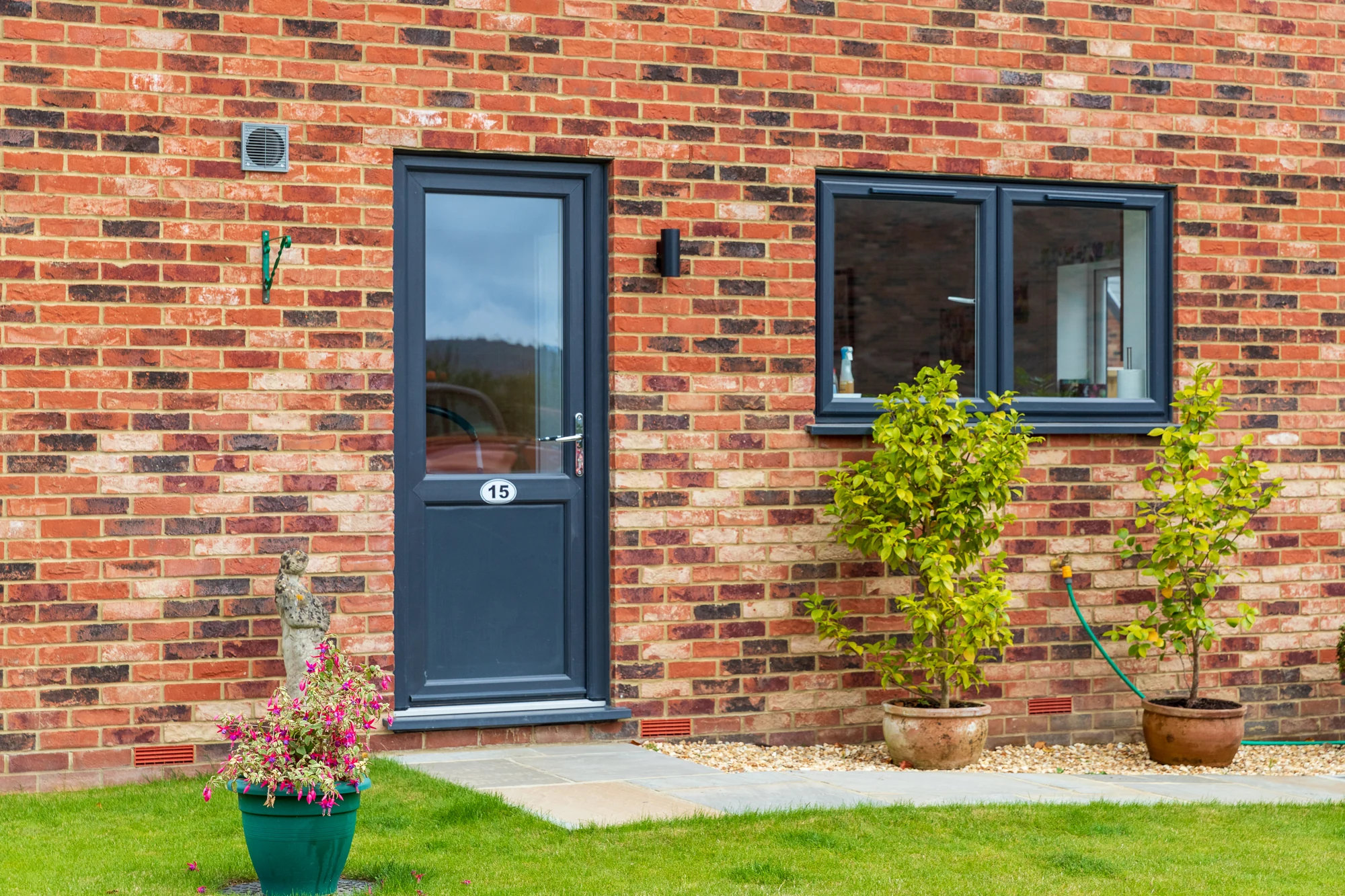 Grey glazed uPVC side door in a red-brick house beside matching windows
