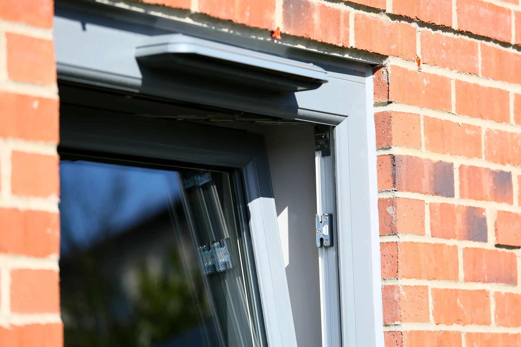 Grey uPVC tilt-and-turn window tilted inward in a brick opening